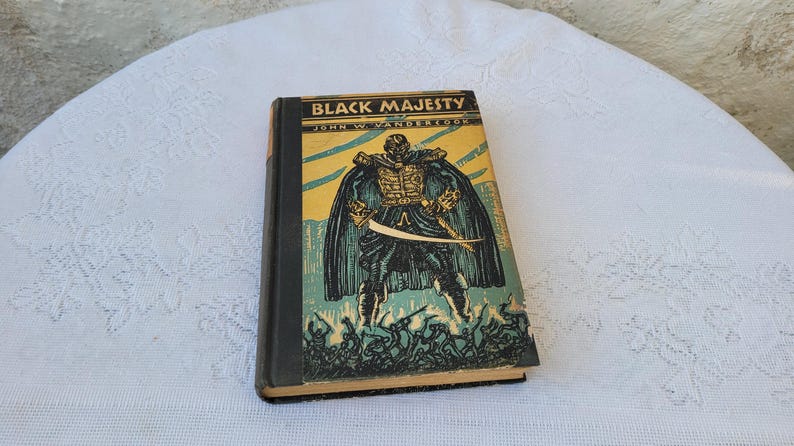 May include: A vintage hardback book titled "Black Majesty" by John W. Vandercook. The cover features a black and white illustration of a man in a cape and holding a sword.