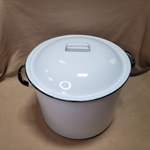 May include: A white enamel pot with a matching lid. The pot has black handles and a black rim. The lid has a small handle. The pot is likely used for cooking and has a classic, vintage look.