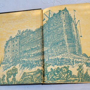 May include: An open book with a yellowed page background and a blue and white illustration of a castle with people surrounding it. The illustration is on both pages of the book.
