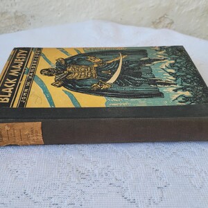May include: A vintage hardback book titled "Black Majesty" by John W. Vandercook. The book cover features a colourful illustration of a man in a black cloak holding a sword.