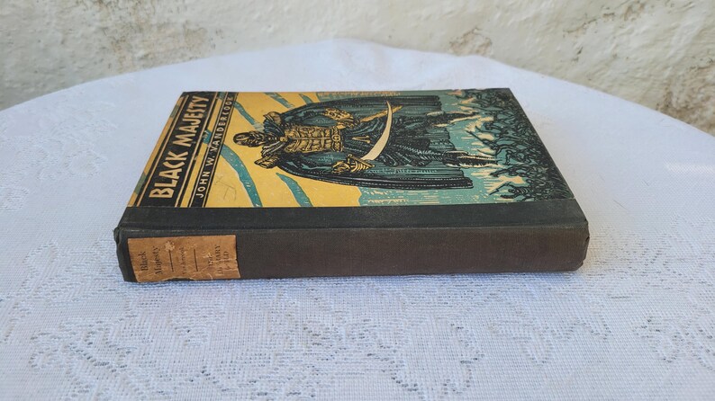 May include: A vintage hardback book titled "Black Majesty" by John W. Vandercook. The book cover features a colourful illustration of a man in a black cloak holding a sword.