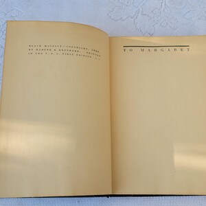 May include: An open book with a cream-coloured cover and pages. The left page has text that reads "BLACK MAGIC" COPYRIGHT 1948 BY WARNER & BROTHERS, PRINTED IN THE U.S.A. FIRST EDITION." The right page has the text "TO MARGARET" printed in black.