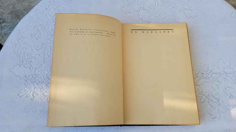 May include: An open book with a cream-coloured cover and pages. The left page has text that reads "BLACK MAGIC" COPYRIGHT 1948 BY WARNER & BROTHERS, PRINTED IN THE U.S.A. FIRST EDITION." The right page has the text "TO MARGARET" printed in black.