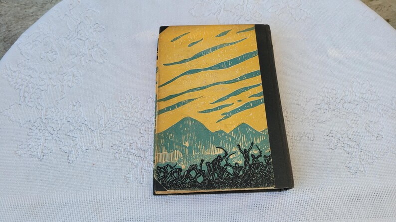 May include: A vintage hardback book with a yellow cover and a black spine. The cover features a green and blue illustration of a mountain range with a sky filled with clouds.