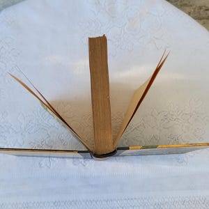 May include: A vintage hardback book with a brown spine and yellowed pages. The book is open and the pages are fanned out.