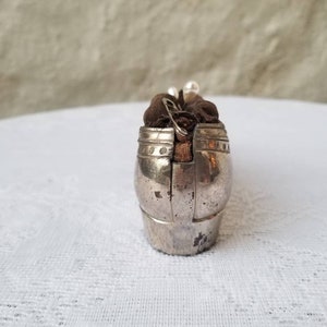 Pode incluir: Uma caixa de metal prateada em forma de sapato com um forro de tecido marrom. A caixa tem uma tampa com dobradi&ccedil;as e um design decorativo.