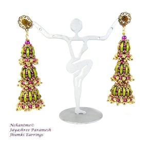 May include: A pair of green and pink jhumki earrings with gold accents. The earrings are hanging from a metal stand.