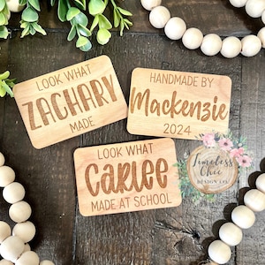 May include: Three wooden signs with personalized text. The first sign says "Look What Zachary Made". The second sign says "Handmade By Mackenzie 2024". The third sign says "Look What Carlee Made At School".