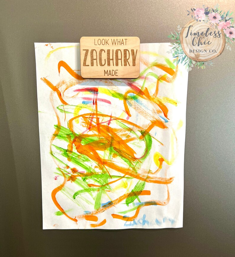 May include: A wooden sign with the text "Look What Zachary Made" on a white background. The sign is attached to a white sheet of paper with colorful abstract artwork on it.