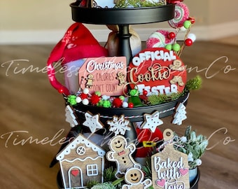 May include: A three-tiered tiered tray decorated for Christmas with gingerbread cookies, a gingerbread house, and signs that say "Gingerbread Baking Co.", "Christmas Calories Don't Count", "Official Cookie Tester", and "Baked with Love".