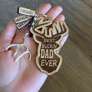 Peut inclure: Porte-cl&eacute;s en bois avec un motif de t&ecirc;te de cerf et le texte "Best Buckin' Dad Ever". Le porte-cl&eacute;s comprend &eacute;galement trois petites &eacute;tiquettes en bois avec les noms "Zachary", "Mackenzie" et "Madison".