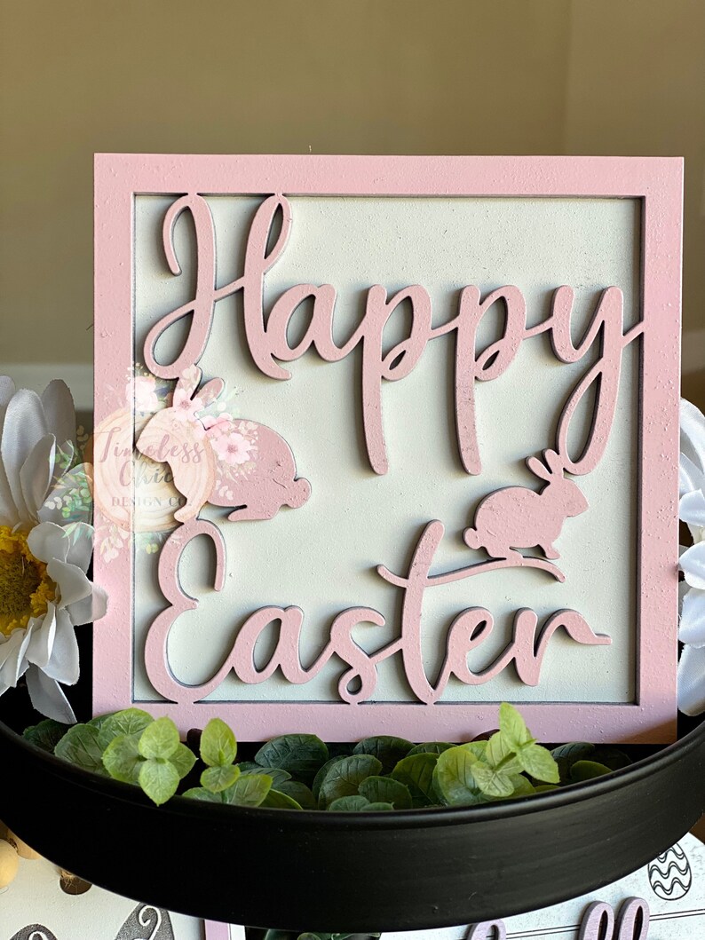 May include: A pink wooden sign with the words "Happy Easter" in white lettering. The sign is decorated with two pink bunny rabbits.