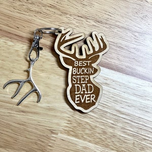 Peut inclure: Porte-cl&eacute;s en bois en forme de t&ecirc;te de cerf avec le texte "Best Buckin Step Dad Ever" grav&eacute; dessus. Le porte-cl&eacute;s est attach&eacute; &agrave; un charme en forme d'antenne en m&eacute;tal argent&eacute;.