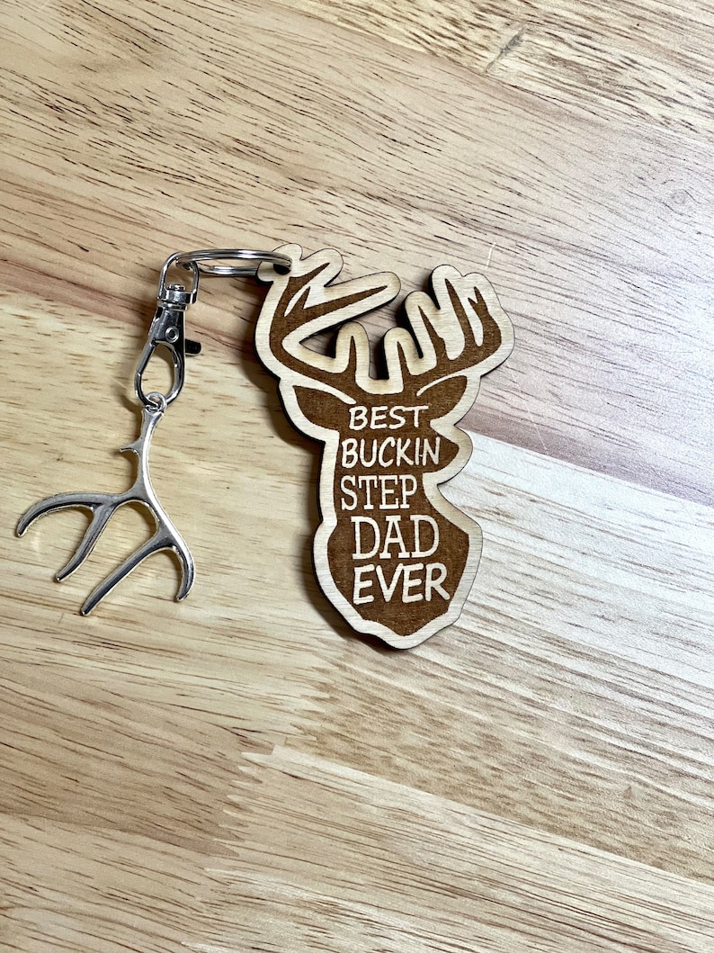 Peut inclure: Porte-cl&eacute;s en bois en forme de t&ecirc;te de cerf avec le texte "Best Buckin Step Dad Ever" grav&eacute; dessus. Le porte-cl&eacute;s est attach&eacute; &agrave; un charme en forme d'antenne en m&eacute;tal argent&eacute;.