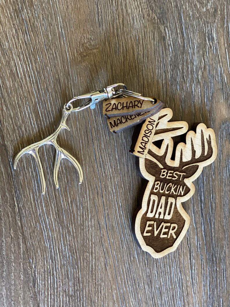 Peut inclure: Porte-cl&eacute;s en bois avec une silhouette de cerf et le texte "Best Buckin' Dad Ever". Trois &eacute;tiquettes en bois avec les noms "Zachary", "Mackenzie" et "Madison" sont attach&eacute;es au porte-cl&eacute;s.