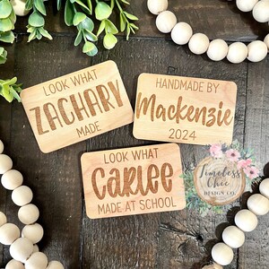 May include: Three wooden signs with engraved text. The first sign says "Look What Zachary Made". The second sign says "Handmade By Mackenzie 2024". The third sign says "Look What Carlee Made At School".