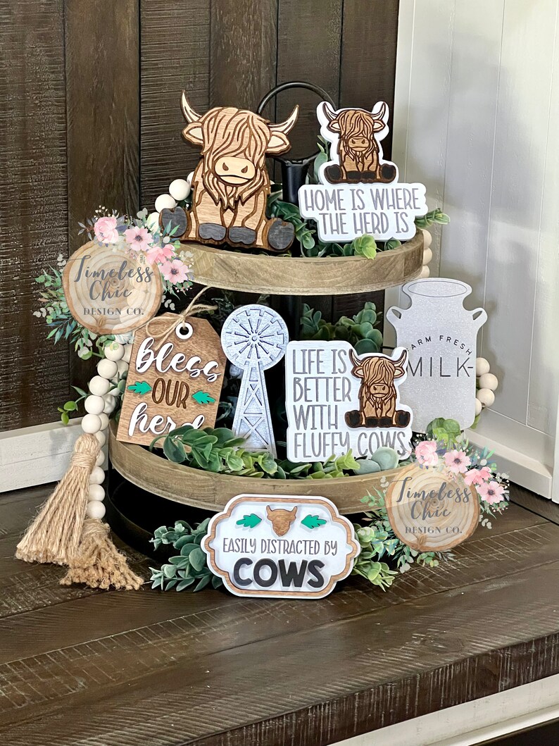 May include: A tiered tray decorated with wooden signs and figurines featuring a cow theme. The signs say "Home is where the herd is", "Life is better with fluffy cows", "Bless our herd", "Easily distracted by cows", and "Farm Fresh Milk".