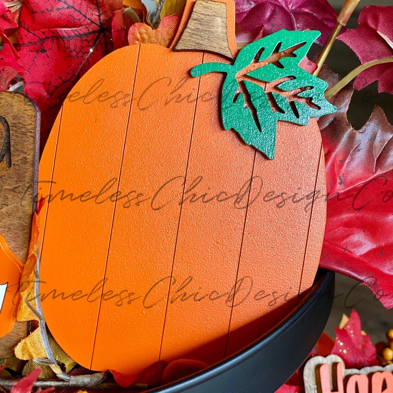 Pode incluir: Corte de madeira em forma de ab&oacute;bora laranja com uma folha verde no topo. A ab&oacute;bora tem uma textura de gr&atilde;o de madeira e &eacute; pintada com uma tinta laranja brilhante. A folha &eacute; pintada de verde brilhante e tem uma superf&iacute;cie ligeiramente texturizada.