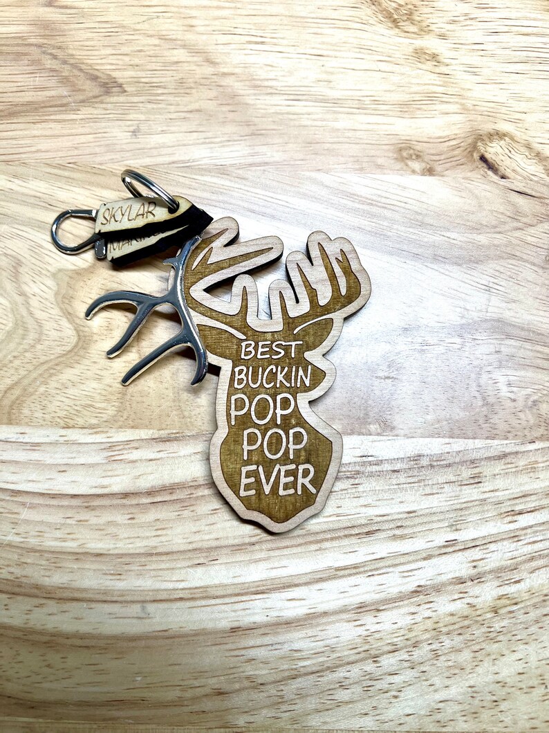 Peut inclure: Porte-cl&eacute;s en bois en forme de t&ecirc;te de cerf avec le texte "Best Buckin' Pop Pop Ever".