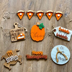 Pode incluir: Um conjunto de decora&ccedil;&otilde;es de A&ccedil;&atilde;o de Gra&ccedil;as de madeira que inclui uma ab&oacute;bora, um peru, uma faixa de torta, uma placa de "Gobble Till You Wobble", uma placa de "Happy Thanksgiving" e uma placa de "I'm Stuffed".