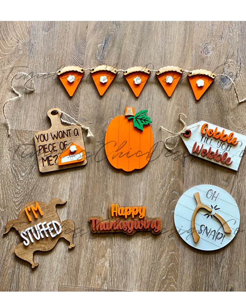 Pode incluir: Um conjunto de decora&ccedil;&otilde;es de A&ccedil;&atilde;o de Gra&ccedil;as de madeira que inclui uma ab&oacute;bora, um peru, uma faixa de torta, uma placa de "Gobble Till You Wobble", uma placa de "Happy Thanksgiving" e uma placa de "I'm Stuffed".