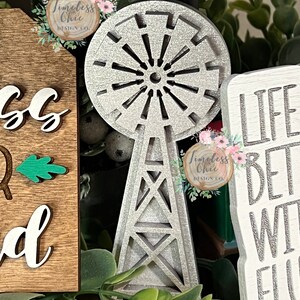 May include: A silver glitter windmill with a wooden base. The windmill is a decorative piece and is surrounded by greenery. The text "Timeless Chic Design Co." is visible on the windmill.