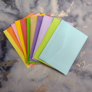 May include: A stack of ten colorful envelopes in various shades of blue, green, yellow, orange, red, and purple. The envelopes are arranged in a fan shape, with the lightest color at the top and the darkest color at the bottom.