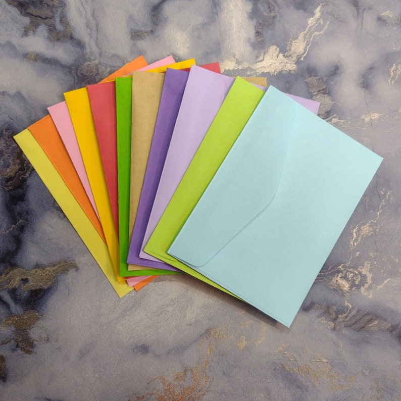 May include: A stack of ten colorful envelopes in various shades of blue, green, yellow, orange, red, and purple. The envelopes are arranged in a fan shape, with the lightest color at the top and the darkest color at the bottom.