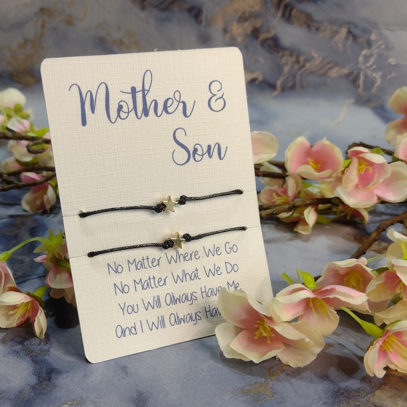 May include: Two black string bracelets with gold star charms on a white card with the text "Mother & Son" and the message "No Matter Where We Go No Matter What We Do You Will Always Have Me And I Will Always Have You".