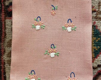 May include: A pink linen tea towel with a white scalloped border. The towel is embroidered with small pink flowers in baskets.