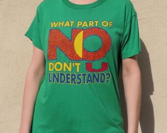 Könnte beinhalten: Ein grünes T-Shirt mit dem Text "WHAT PART OF NO DON'T U UNDERSTAND?" in einem farbenfrohen Design. Das T-Shirt wird von einer Person mit Sonnenbrille getragen.