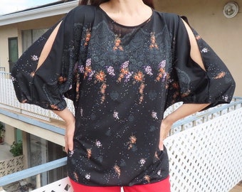 May include: Black blouse with floral pattern and open sleeves. The top has a round neckline and a sheer yoke. The sleeves are long and have a split design. The blouse is paired with red pants.