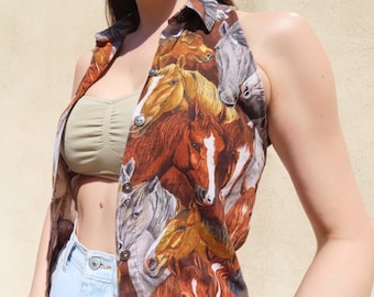 May include: A sleeveless button-down shirt featuring a repeating pattern of horse faces in shades of brown, tan, and white. The shirt has a collared neckline and is buttoned down the front with dark buttons. The shirt is paired with light blue denim jeans.