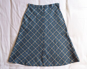 May include: A-line skirt in a blue and tan plaid pattern. The skirt has a fitted waist and flares out towards the hem. The fabric appears to be a woven material, suitable for cooler weather. The skirt is laid flat on a white surface.