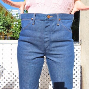 May include: Blue denim jeans with a high waist and classic five-pocket design. The jeans have copper-colored rivets and stitching. The denim is a medium wash, and the jeans appear to be unworn.