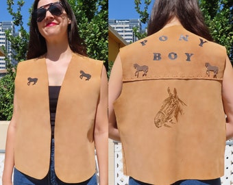 May include: Tan suede vest with horse silhouettes and the text "PONY BOY". The vest features a horse head design on the back. A stylish, open-front vest for a western or equestrian theme.