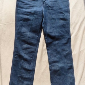 May include: A pair of blue denim jeans with a classic five-pocket design. The jeans have a button and zipper closure, along with copper-colored rivets and stitching. The jeans are laid flat on a light-colored surface.