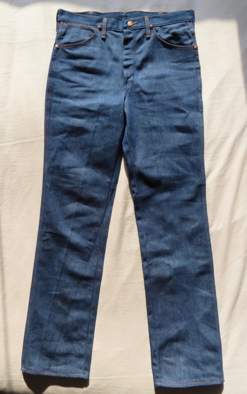 May include: A pair of blue denim jeans with a classic five-pocket design. The jeans have a button and zipper closure, along with copper-colored rivets and stitching. The jeans are laid flat on a light-colored surface.