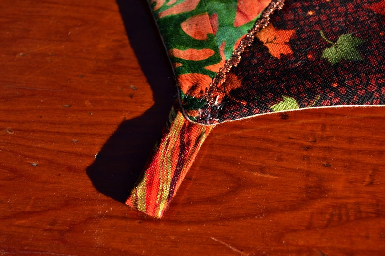 May include: Close-up of a colorful fabric with a gold and red trim. The fabric is folded over and sewn together. The fabric is on a wooden surface.