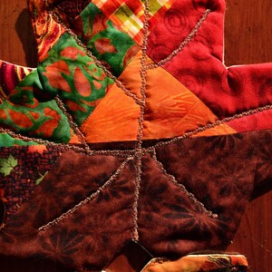 May include: A patchwork leaf-shaped quilt block with a variety of colorful fabrics, including red, orange, green, and brown. The fabric is sewn together in a geometric pattern and the edges are trimmed with gold thread.