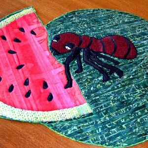 May include: A red and black ant crawling on a green and white watermelon-shaped fabric. The watermelon is cut open and the ant is crawling on the inside of the watermelon.