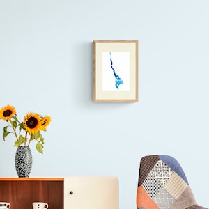 May include: A framed watercolor painting of a blue abstract shape resembling a river or stream. The painting is hanging on a light blue wall above a wooden cabinet and a patterned chair.