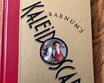 Può includere: Un libro dorato con il titolo "Barnum's Kaleidoscope" sulla copertina. La copertina presenta una foto di due clown in una cornice circolare. Un biglietto per lo spettacolo è attaccato alla copertina. Il biglietto recita "Ringling Bros. Presents Barnum's Kaleidoscope" e "Thu Sep 14 2000 7:30PM".