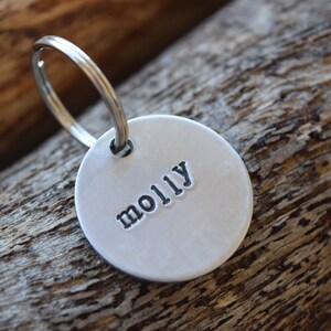 Puede incluir: Llavero de plata con una etiqueta redonda que dice "molly" en letras negras.