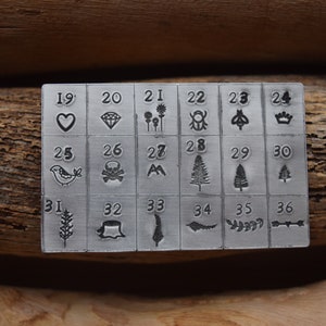 K&ouml;nnte beinhalten: Ein Stempelset aus Metall mit 36 verschiedenen Designs, darunter Herzen, Diamanten, Blumen, K&auml;fer, Kronen, V&ouml;gel, Totenk&ouml;pfe, Berge, B&auml;ume, Weizen und einen Baumstumpf. Die Zahlen 19 bis 36 sind &uuml;ber jedem Design aufgedruckt.