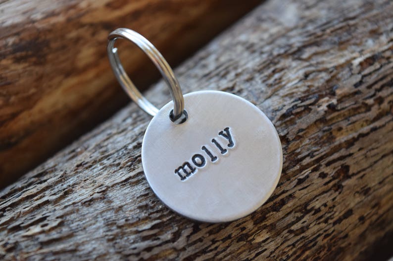 Puede incluir: Llavero de plata con una etiqueta redonda que dice "molly" en letras negras.
