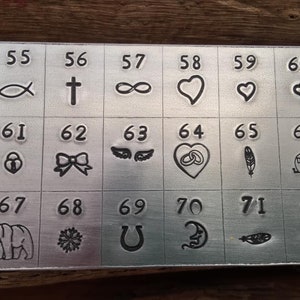 K&ouml;nnte beinhalten: Eine Metallplatte mit 72 verschiedenen Symbolen und Zahlen. Die Symbole umfassen einen Fisch, ein Kreuz, ein Unendlichkeitszeichen, ein Herz, eine Schleife, Fl&uuml;gel, einen Ring, eine Feder, einen Wohnwagen, einen B&auml;ren, eine Schneeflocke, ein Hufeisen, einen Halbmond, eine Feder und einen Schnurrbart.