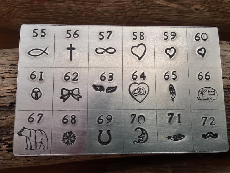 K&ouml;nnte beinhalten: Eine Metallplatte mit 72 verschiedenen Symbolen und Zahlen. Die Symbole umfassen einen Fisch, ein Kreuz, ein Unendlichkeitszeichen, ein Herz, eine Schleife, Fl&uuml;gel, einen Ring, eine Feder, einen Wohnwagen, einen B&auml;ren, eine Schneeflocke, ein Hufeisen, einen Halbmond, eine Feder und einen Schnurrbart.