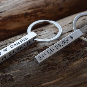 May include: Two silver keychains with engraved bars. One bar reads "AMY ♥ DANIEL XX.IV.XI.MMXII" and the other reads "24° 51' 26.02" S".