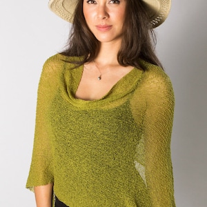 Op de afbeelding: Een chartreuse groene gebreide poncho met een colkraag en een losse, semi-transparante textuur. Het kledingstuk heeft een asymmetrische zoom en korte mouwen, wat een lichte laag over een zwart topje vormt, gecombineerd met een beige en zwarte zonnehoed.